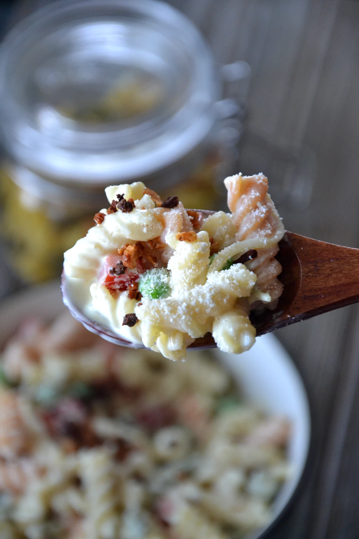 bite shot view of mac salad on wooden spoon topped with fake bacon bits.