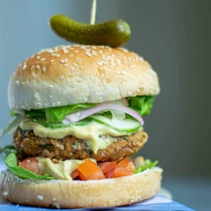 a stacked burger with toppings and sauce and a toothpick with a pickle on top.