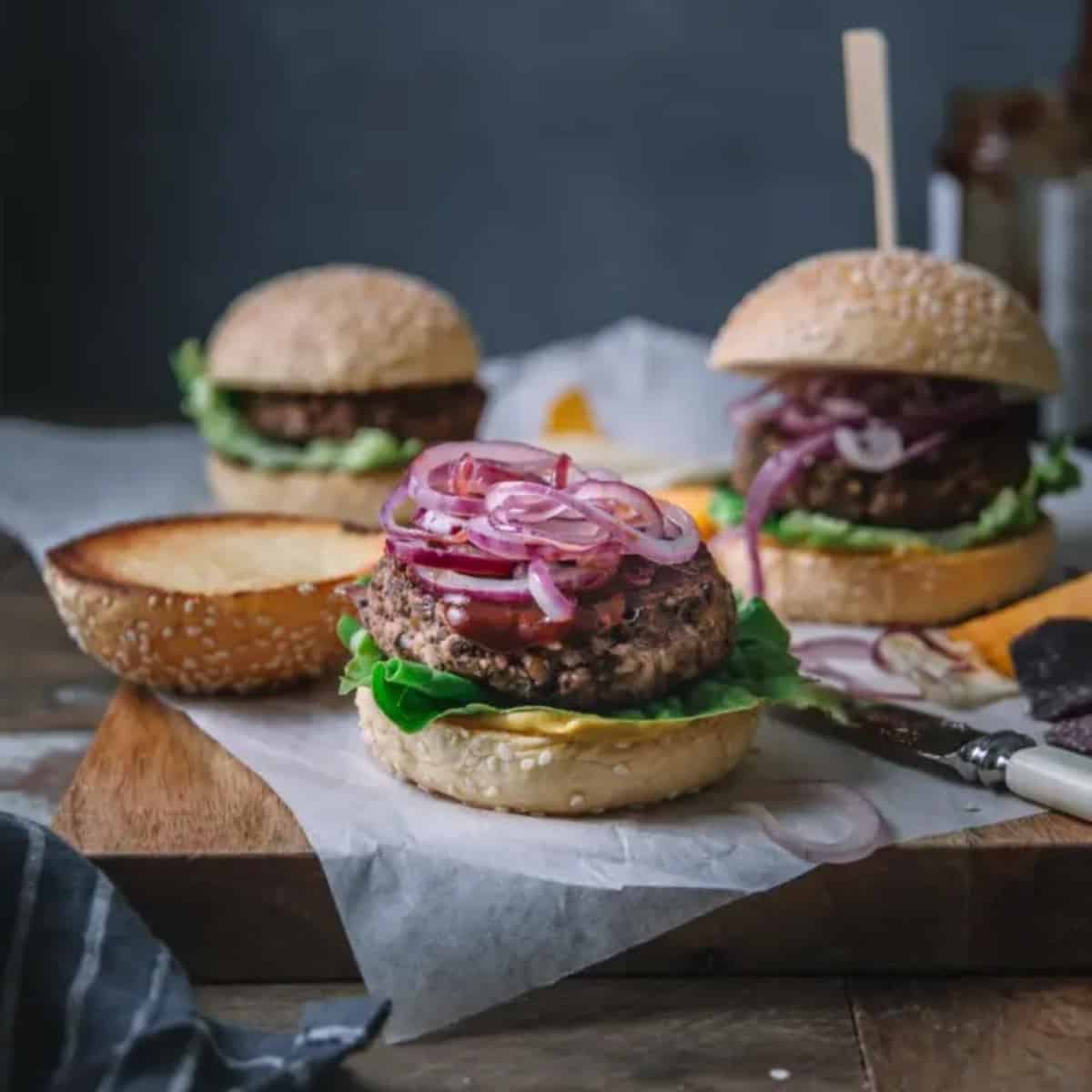black bean burgers topped with red onion and sauce with other burgers in background.