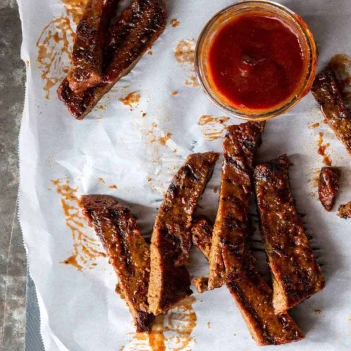 saucy vegan bbq ribs displayed with a side of bbq sauce.
