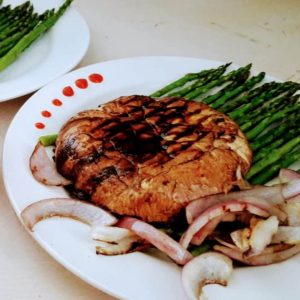 a grilled portobella mushroom on a plate with asparagus and onions.