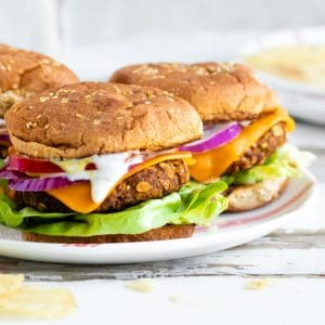 three chickpea burgers on a plate with buns and toppings.