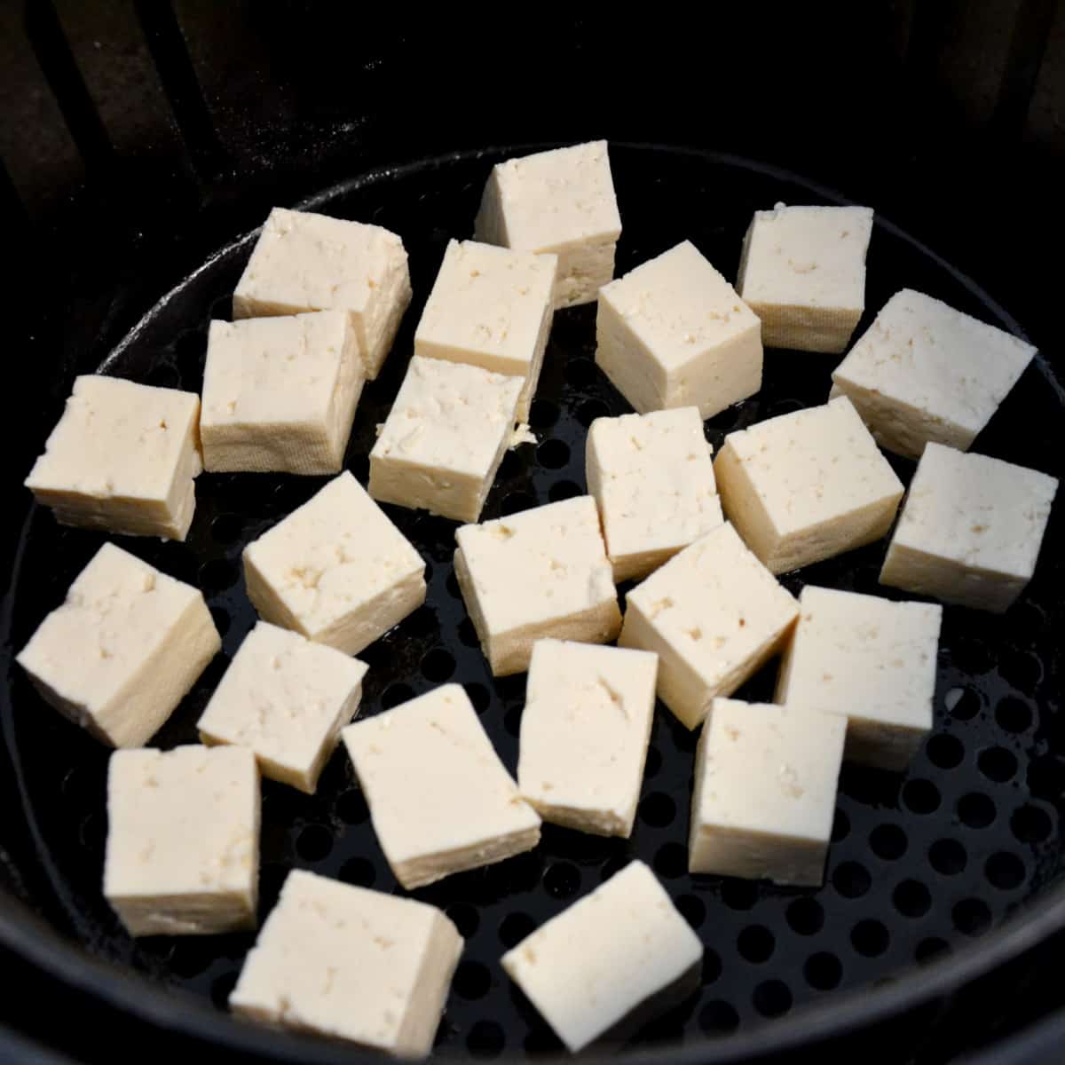 placing raw tofu into basket of air fryer.