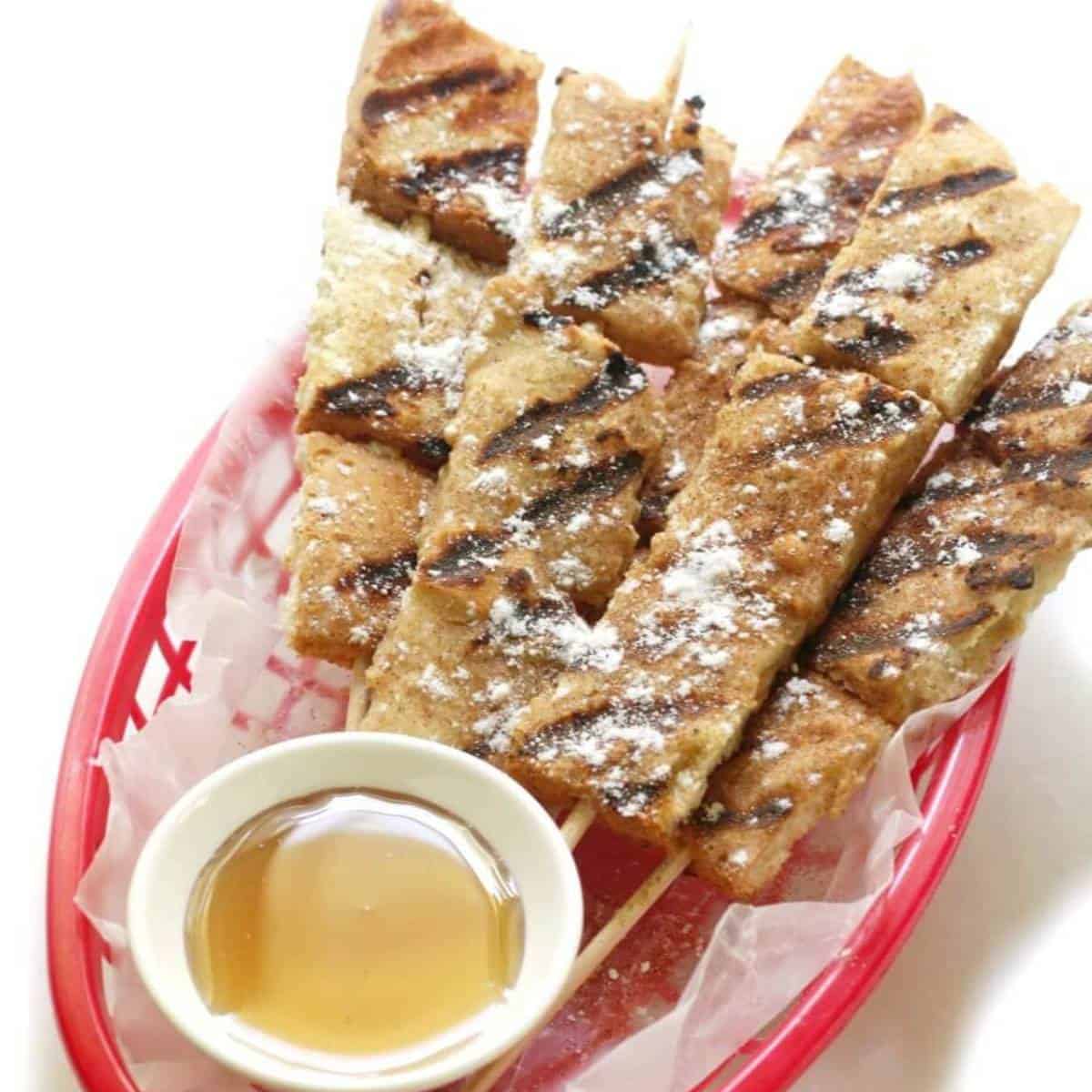 french toast sticks on skewers dusted with powder sugar and maple syrup for dipping.