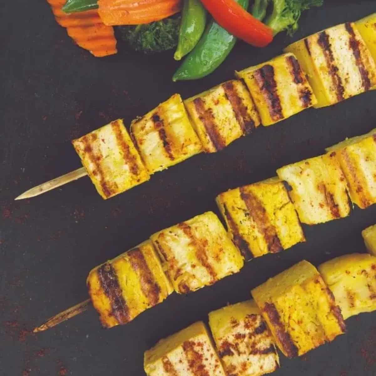 tofu grilled to perfection on skewers with veggies off to side.