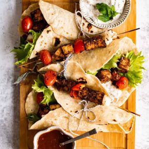 four skewers wrapped in tortillas with sauce.