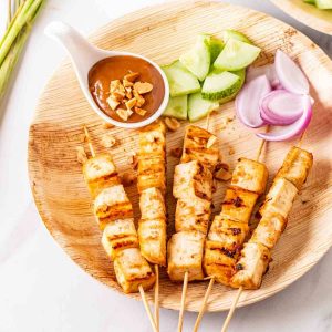 peanuts and dipping sauce with skewers on wooden plate.