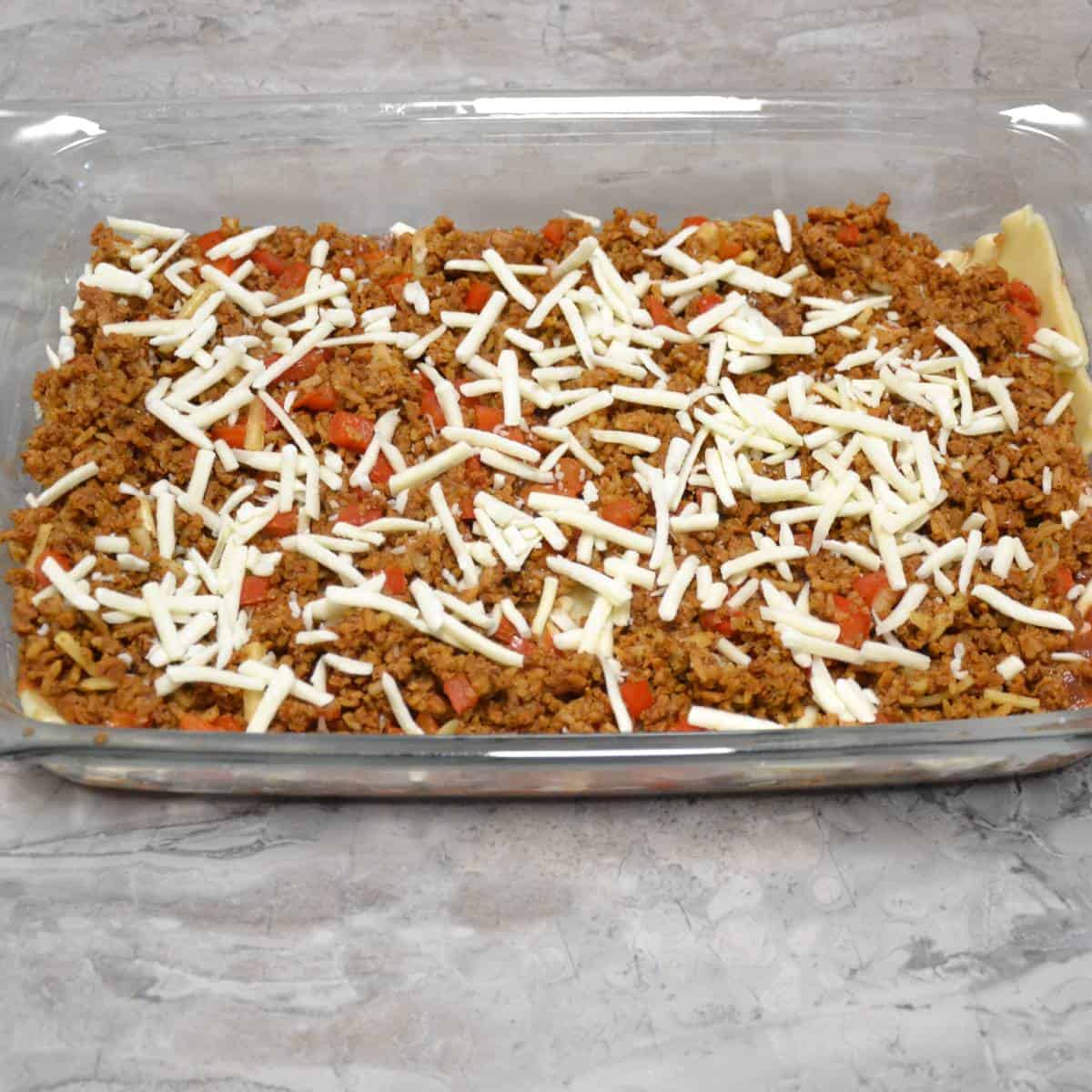 baking dish with noodles and stuffed pepper mixture layered for step sixteen.