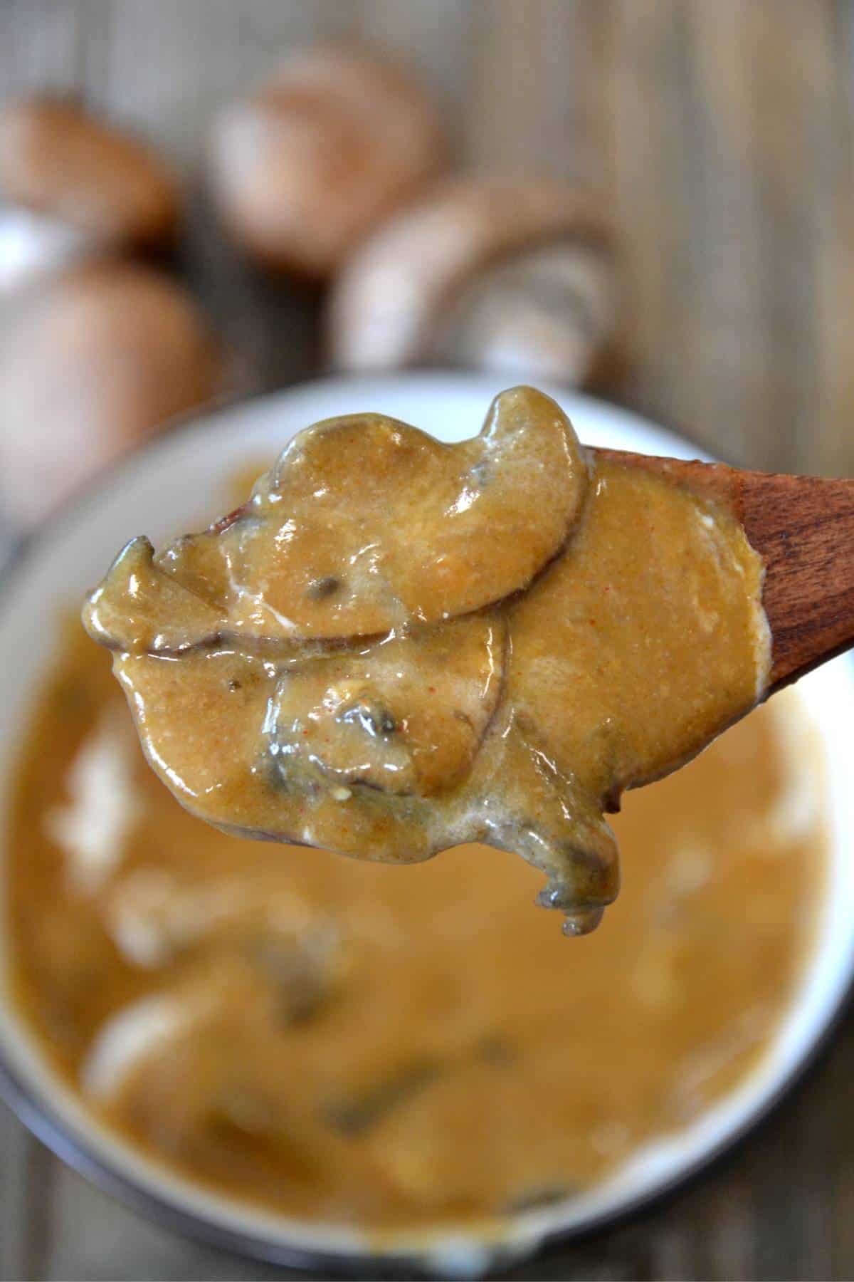 wooden spoon holding mushrooms in a creamy sauce.