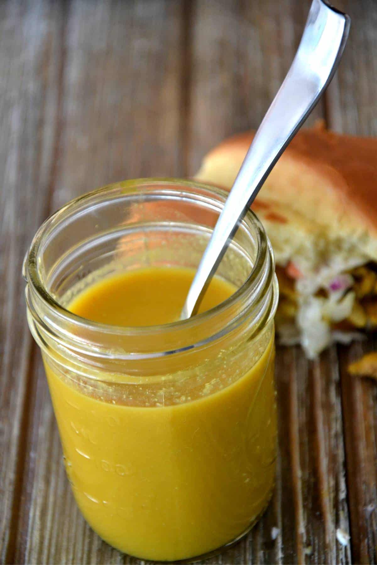 mustard sauce with spoon and sandwich in background.