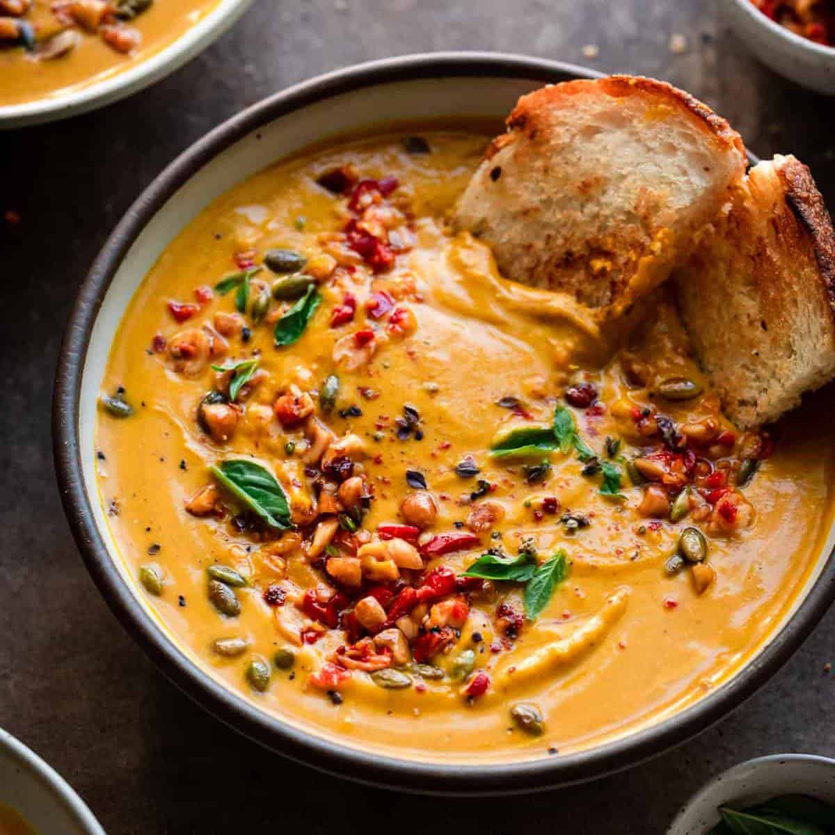 vibrant orange soup with bread and toppings that contrast the orange.