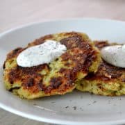 zucchini fritters on white plate topped with dill sour cream sauce.