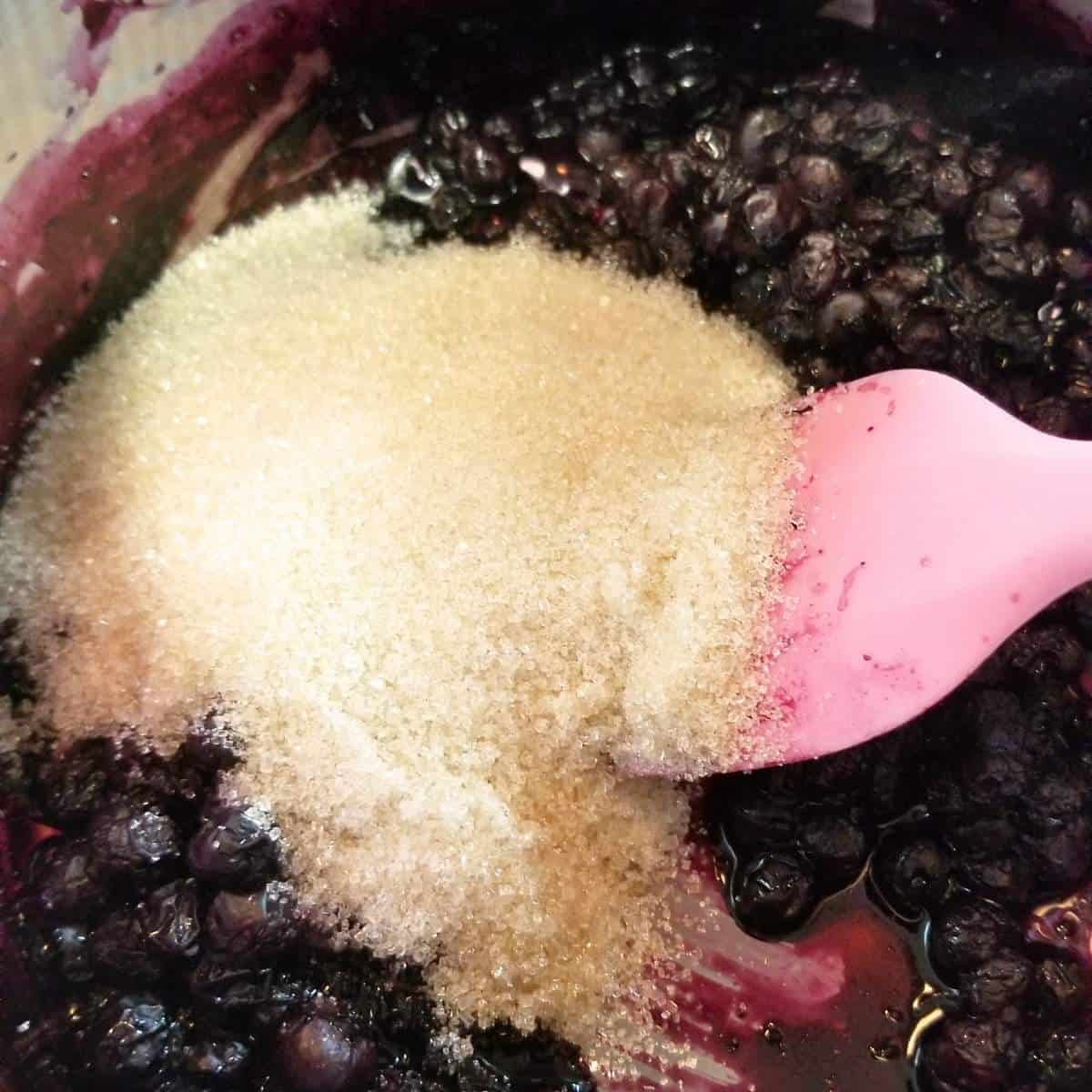 step six adding sugar to the blueberries while still cooking in pot.