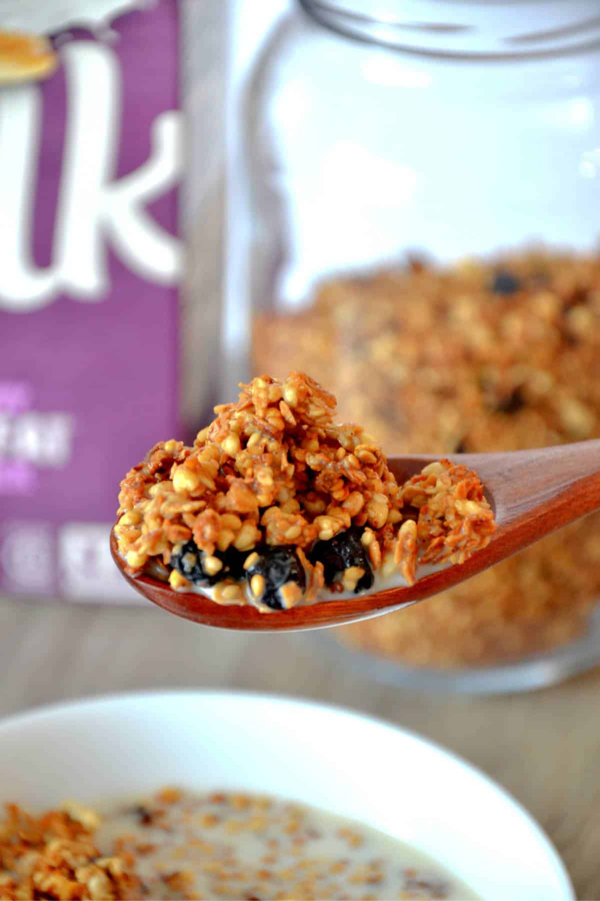 blueberry granola on a wooden spoon with oat milk.