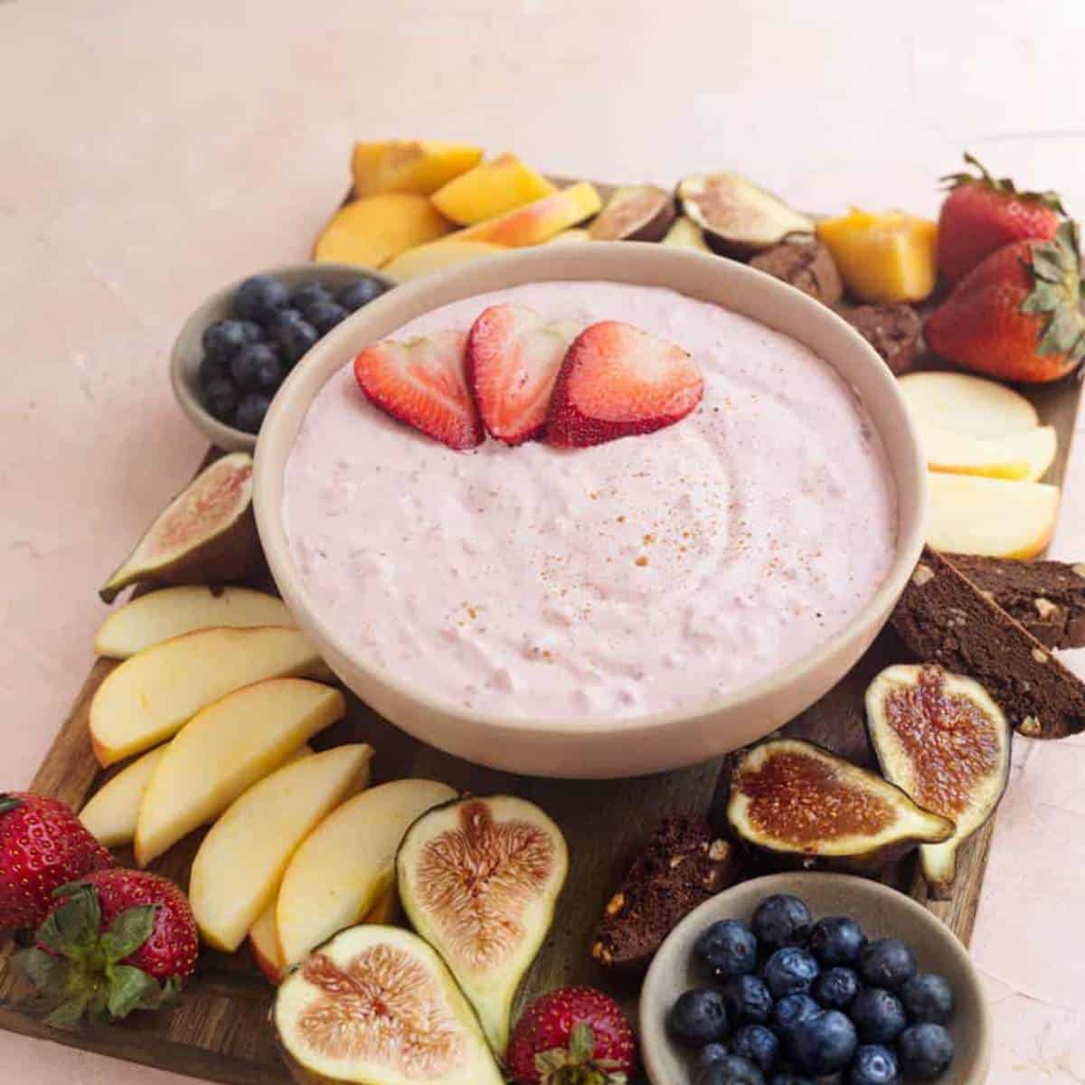 bowl of fruit dip with fruits displayed around the bowl on a wooden board.