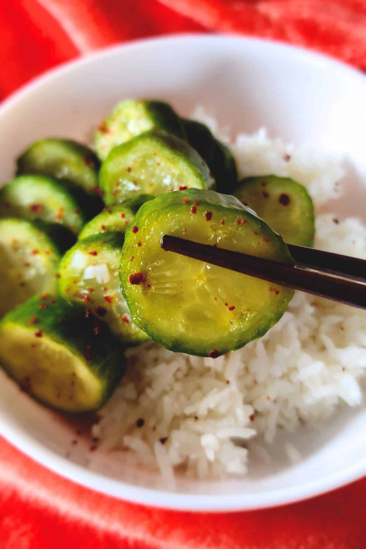 chopsticks holding a cucumber coin with bowl in background.
