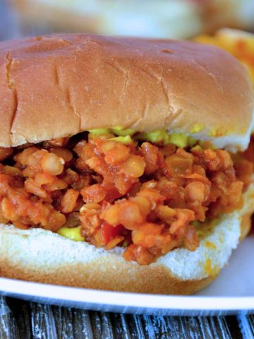 lentil sloppy joe on a white plate with mustard between two buns.